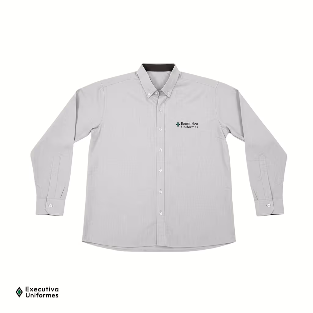 Camisa social de manga longa na cor cinza claro com textura sutil. Apresenta fechamento frontal por botões brancos, gola com botões de fixação nas pontas (estilo button-down), punhos abotoados, detalhe em tecido escuro na parte interna do colarinho e um logotipo bordado no lado esquerdo do peito.